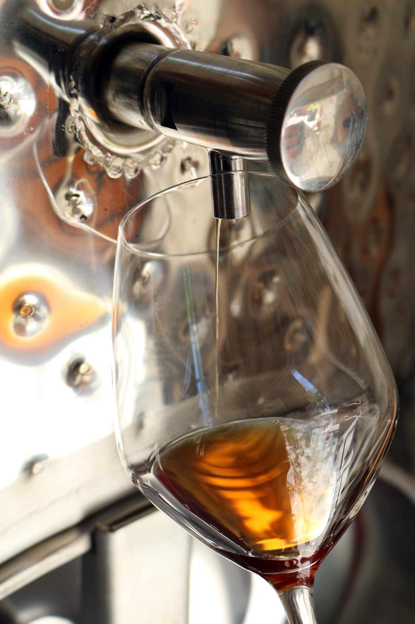 Golden Commandaria wine being poured into a glass from a steel tank.